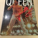 Fotografie znázorňuje přebal albumu nebo knihy s nápisem QUEEN a červeným rukopisným textem Best Of. Na snímku je zobrazen zpěvák s mikrofonem v bílý…