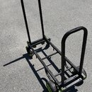 Černý transportní vozík s kovovou konstrukcí a čtyřmi pneumatickými koly. Rám má obdélníkový tvar s dvěma vyklápěcími madly a zelenými detaily u spoj…