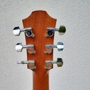 Zadní strana hlavy akustické kytary z hnědého dřeva s chromovanými ladicími mechanismy. Na horních dvou mechanismech je vidět kulaté logo s písmeny J…