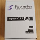 Bílá papírová krabice s nápisy. V horní části je fialové logo a text Two notes AUDIO ENGINEERING. Uprostřed je černý pruh s bílým textem Torpedo C.A.…