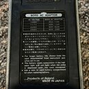 Fotografie zachycuje zadní stranu kytarového pedálu v kovovém šasi s černým plastovým krytem. Na štítku je uveden nápis BOSS AC ADAPTOR a tabulka s h…