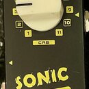 Černý efekt pedál s bílým otočným knoflíkem a malým černým trimrem u nápisu VOL. Na zařízení jsou žluté popisky DC 9V, USB, XLR a CAB, přičemž kolem…