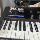 Černý klávesový syntetizátor s bílými a černými klávesami. Na horním panelu je bílý nápis Roland a modelové označení JX-3P s doplňkem PROGRAMMABLE 6-…