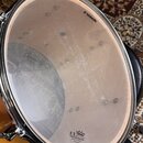Fotografie znázorňuje průhledný buben na bubnu s kovovým obručem. Na povrchu jsou vidět nápisy SONOR v horní části a REMO UX DRUM HEAD MADE BY REMO I…