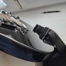 Detailní pohled na spodní část černého trupu elektrické kytary s lesklým povrchem. Je vidět kovový most a černý popruh připevněný k nástroji. Na povr…