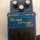 Modrý efekt pedál s nápisy Blues Driver a BD-2. Na spodním černém spínači je vyražené logo BOSS. Horní část obsahuje tři ovládací knoflíky s popisky…