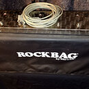 Černý krycí povlak s bílým nápisem ROCKBAG by Warwick. Na povlaku leží kovový panel s ovládacími prvky a zapojeným bílým kabelem. Na panelu jsou vidě…