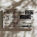 Bílý analogový syntetizátor s nápisem UDO SUPER 6. Přední panel obsahuje zahlreiche černé a bílé ovratové knofíky, posuvníky a přepínače rozdělené do…