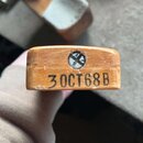 Detailní pohled na dřevěný díl světle hnědé barvy. Na povrchu je vyražen černý nápis 30CT68B a nad ním se nachází kulatý kovový šroub. Povrch dřeva v…