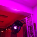 Fotografie zobrazuje řadu osvětlovacích efektů namontovaných na hliníkovém trussu. V popředí je černý pohyblivý reflektor typu moving head, který sví…