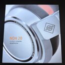 Fotografie znázorňuje detail stříbrných studiových sluchátek. Na rámu je nápis NEUMANN.BERLIN a STUDIO HEADPHONE NDH 20, na boku je logo značky Neuma…