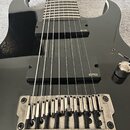 Černá elektrická kytara s osmi strunami a dvěma černými snímači s bílým nápisem EMG. Stříbrný kobylník má na pravé straně vyrytý nápis Floyd Rose. Po…
