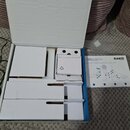 Otevřená modro-bílá krabice s vložkami z bílého kartonu. Vedle krabice leží návod s logem AKG a nápisem WMS40 MINI DUAL. Vnitřek krabice je prázdný,…