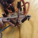 Detailní pohled na vnitřní elektroniku přístroje s viditelnými součástkami, kondenzátory a tlustými měděnými vodiči. V popředí je kovová deska s přiš…