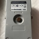 Záběr na spodní stranu stříbrného efekt pedálu z kovu. Na bílém štítku je uveden nápis tc electronic, DESIGNED IN DENMARK a BATTERY. Štítek obsahuje…