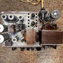 Fotografie zachycuje vnitřní elektronické zapojení zařízení na kovovém šasi. Jsou zde vidět různé komponenty, včetně několika vakuových elektronek, v…