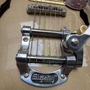 Detailní pohled na chromovaný vibrační mechanismus Bigsby na hnědé elektrické kytáře. Na spodní části mechanismu je nápis Bigsby® LICENSED. Povrch ch…