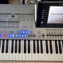 Stříbrný digitální klavír s vyklopeným displejem, na kterém je nápis Tyros 5 a text Program Version: 2.02, Standalone Ed.1.03 (14427/10) a v dolní čá…