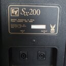 Detail zadní strany černého reproduktorového boxu s informačním štítkem. Na štítku je uvedeno logo EV, model Sx200, Nominal Impedance: 8 Ohms a Power…