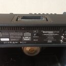 Zadní strana černého kytarového komba s texturovaným povrchem. Na zadním panelu je bílý nápis MUSTANG GT100 a text FENDER MUSICAL INSTRUMENTS CORP. V…