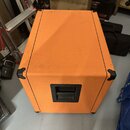 Kutý kytarový kombozesilovač nebo box potažený oranžovým textilem s černými plastovými rohy. Na přední straně je umístěna černá plastová rukojeť. Pov…