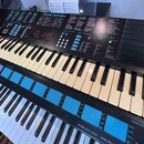 Černý digitální klavír s bílými a černými klávesami. Na horním panelu jsou nápisy MUSIC STATION, FM VOICE BANK / PCM a PERCUSSION SET, dále je vidět…