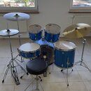 Modrá bicí souprava s chromovaným kováním, která obsahuje snare drum, dva tom-tomy, bass drum a dva činely. Na stěnách kotlů nejsou viditelné žádné z…