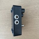 Fotografie zachycuje boční pohled na černý kytarový efekt v kovovém krytu. Na boku jsou umístěny dva kovové 6,35mm jack konektory a jeden malý stříbr…