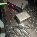 Na fotografii jsou dvě černá elektronická zařízení a připojovací kabel. Větší jednotka má nápisy eTone, Wireless System a digitální displej zobrazují…
