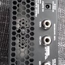 Zadní strana černého kytarového komba s kovovou mřížkou v六úhelníkovém vzoru. Na šasi jsou nápisy PEAVEY ELECTRONICS CORPORATION, DESIGNED AND ENGINEE…