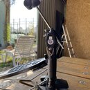 Černý basový pedál z kovu s kovovými mechanismy a pružinou. Na plošince je vidět bílý nápis s logem, ze kterého je čitelné slovo "TAMA". Povrch pedál…