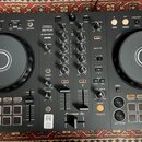 Černý DJ kontrolér s dvěma jog-koly a centrálním mixážním sekcí. Na přístroji jsou viditelné nápisy PERFORMANCE DJ CONTROLLER, DDJ-FLX4, rekordbox a…