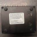 Fotografie zachycuje spodní stranu černého elektronického zařízení s kovovým povrchem. Uprostřed je bílá nálepka s anglickým a francouzským textem za…