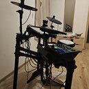 Elektronická bicí souprava v černé barvě s několika pady a činely. Na spodním rámu je viditelný nápis ALESIS. Souprava obsahuje ovládací modul s modř…
