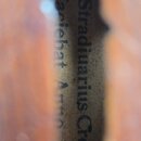 Detailní pohled na štítek uvnitř těla smyčcového nástroje. Na štítku je černý nápis „Stradiuarius Cremonens“ a v druhém řádku „Facebat Anno 176“. Pap…