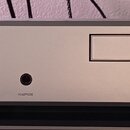 Stříbrný audio komponent s digitálním displejem, na kterém svítí zelený nápis AM 7.28. Na pravé straně je logo v kruhu a nápis LINN, v dolní části je…