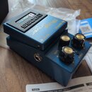 Modrý efekt pedál s nápisy BOSS, WAZA CRAFT a Blues Driver BD-2W. Zařízení má tři černé otočné knoflíky s kovovými vršky a popisky GAIN, TONE a LEVEL…