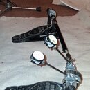 Černý dvojpedál k bicím s kovovými mechanismy a bílými plstěmi na beaterech. Na obou pedálech je nápis IRON COBRA a u levého pedálu je uveden model E…