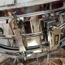 Detailní pohled na chromovaný obal snare bubnu. Na mechanismu jsou vidět nápisy "SONOR" a "Made in Germany". Povrch vykazuje známky používání v podob…