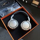 Stříbrná studiová sluchátka s černým náušníkem v oranžovo-černé krabici. Na obou mušlích je nápis STUDIO HEADPHONE 600 a BEHMANN BERLIN. Vedle sluchá…
