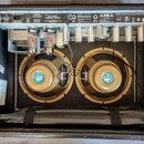 Zadní pohled do otevřeného kytarového komba s dvěma hnědými reproduktory. Na horním ovládacím panelu jsou nápisy 68 CUSTOM VIBROLUX REVERB, FENDER MU…
