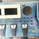 Modrý kytarový syntetizátor s nápisem Roland GR-55 GUITAR SYNTHESIZER. Zařízení obsahuje displej, ovládací tlačítka s popisky jako SOUND STYLE, V-LIN…