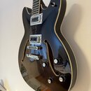 Černá polodublá elektrická kytara s hnědým lemováním a dvěma f-otvory. Na těle jsou dva humbuckery, most s laděním a stoper, čtyři ovládací knofíky a…