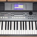 Šedý digitální klavír s nápisem YAMAHA v horní části. V pravém dolním rohu je označení modelu PSR-S570. Nástroj má vestavěný displej, dvě mřížky repr…
