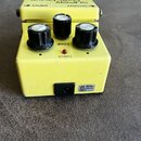 Žlutý efekt pedál s třemi černými ovládacími knoflíky a červenou kontrolkou. Na horní části je nápis SUPER Over Drive SD-1 a označení vstupů INPUT a…