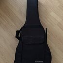 Černý poloměký pouzdro (gig bag) na kytaru s přední kapsou a popruhymi. V dolní části je bílý nápis YAMAHA s doprovodným logem. Povrch materiálu vyka…