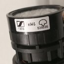 Detailní pohled na černý plastový prvek s bílou nálepkou. Na nálepce je logo značky Sennheiser, nápis e945, číslo 1308 a sériové číslo 538595 vedle s…