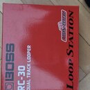 Červená krabice s nápisy BOSS, RC-30 a DUAL TRACK LOOPER. V pravé části je svisle napsáno Loop Station a umístěno logo TWIN PEDAL. Povrch krabice vyk…