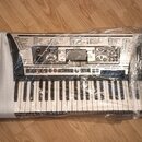 Elektronický klavír značky YAMAHA, model PSR-350, zabalený v průhledné plastové fólii a bílém polystyrenovém obalu. Nástroj je umístěn v kartonových…