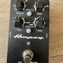 Černý efekt pedál s nápisy Ampeg a CLASSIC Analog Bass Preamp. Zařízení má čtyři černé otočné ovladače s popisky Volume, Bass, Mid a Treble, dva bílé…